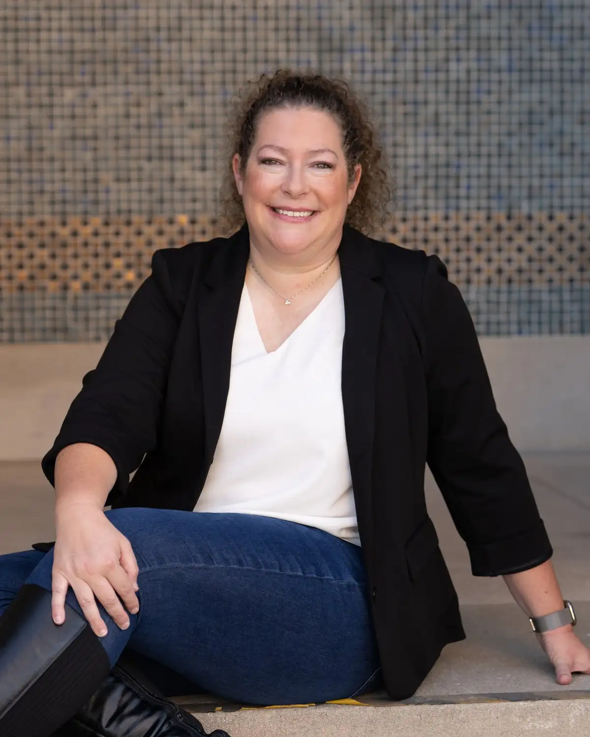 Amanda, onboarding and transactions coordinator at Alpine, seated on stone steps in a black blazer