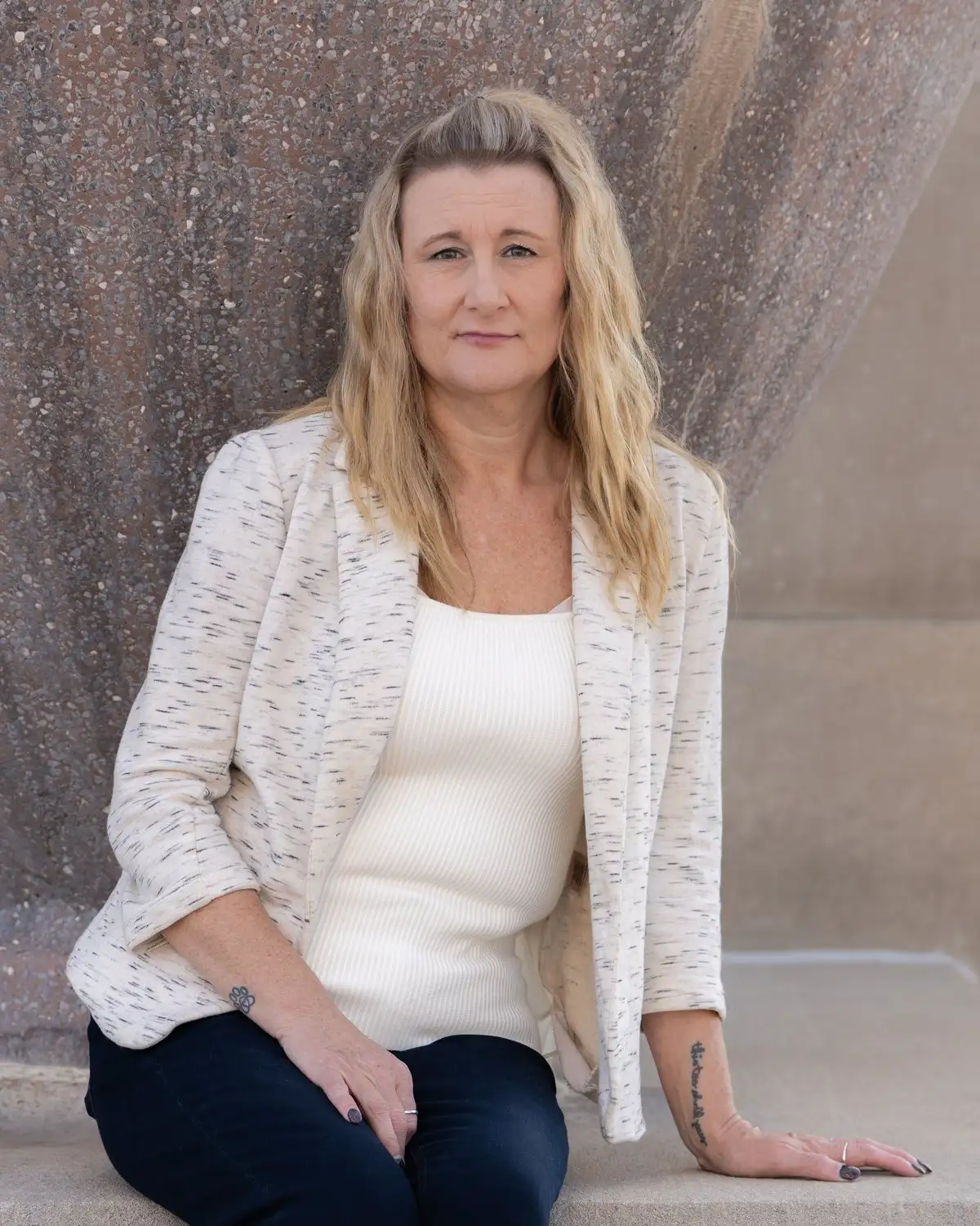 Angie, tenant relations and lead property manager at Alpine, seated on a stone ledge in a cream jacket