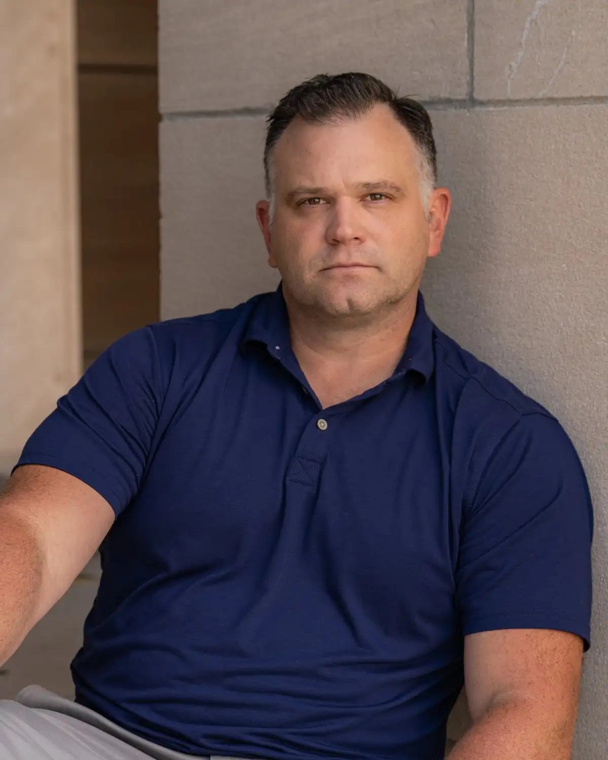 Marcus, founder and owner of Alpine Property Management, seated against a stone wall in a navy polo